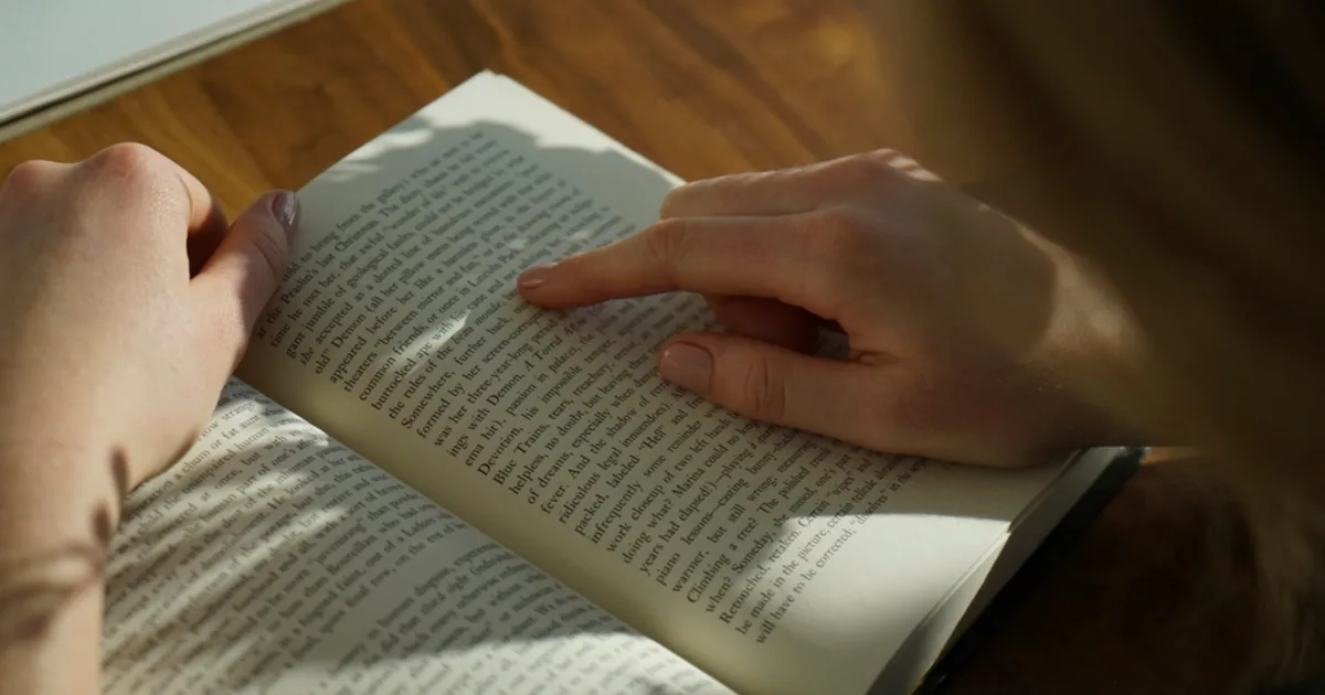 A reader at a wooden desk with an open book, evoking close critical reading.